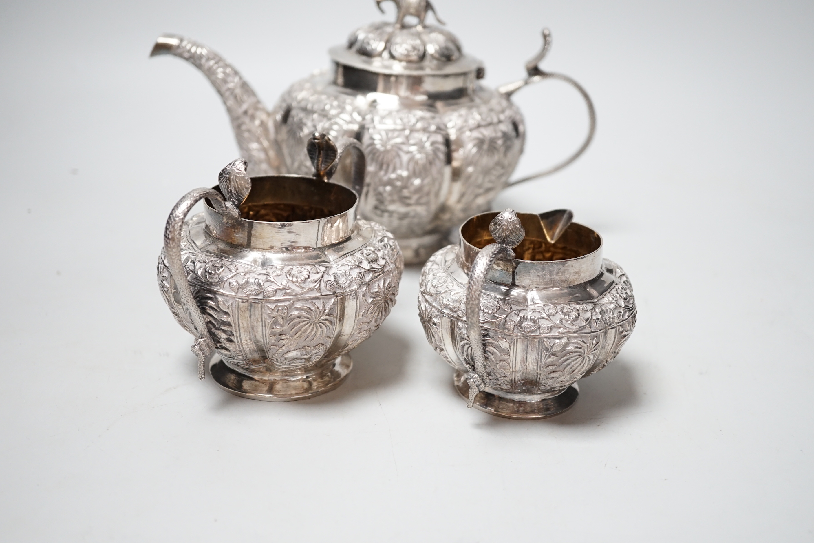 An Indian embossed white metal three piece tea set, with cobra handles and elephant finial, 25.7oz.